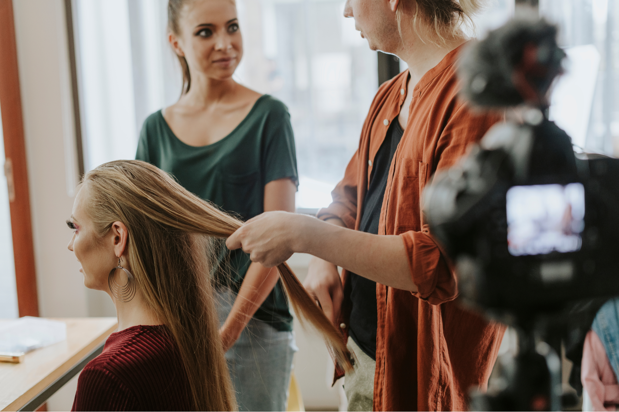 Hairdresser speaking with student while doing client’s hair and recording in hair salon