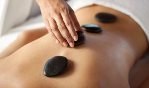 Hand massaging lower back with warm stones