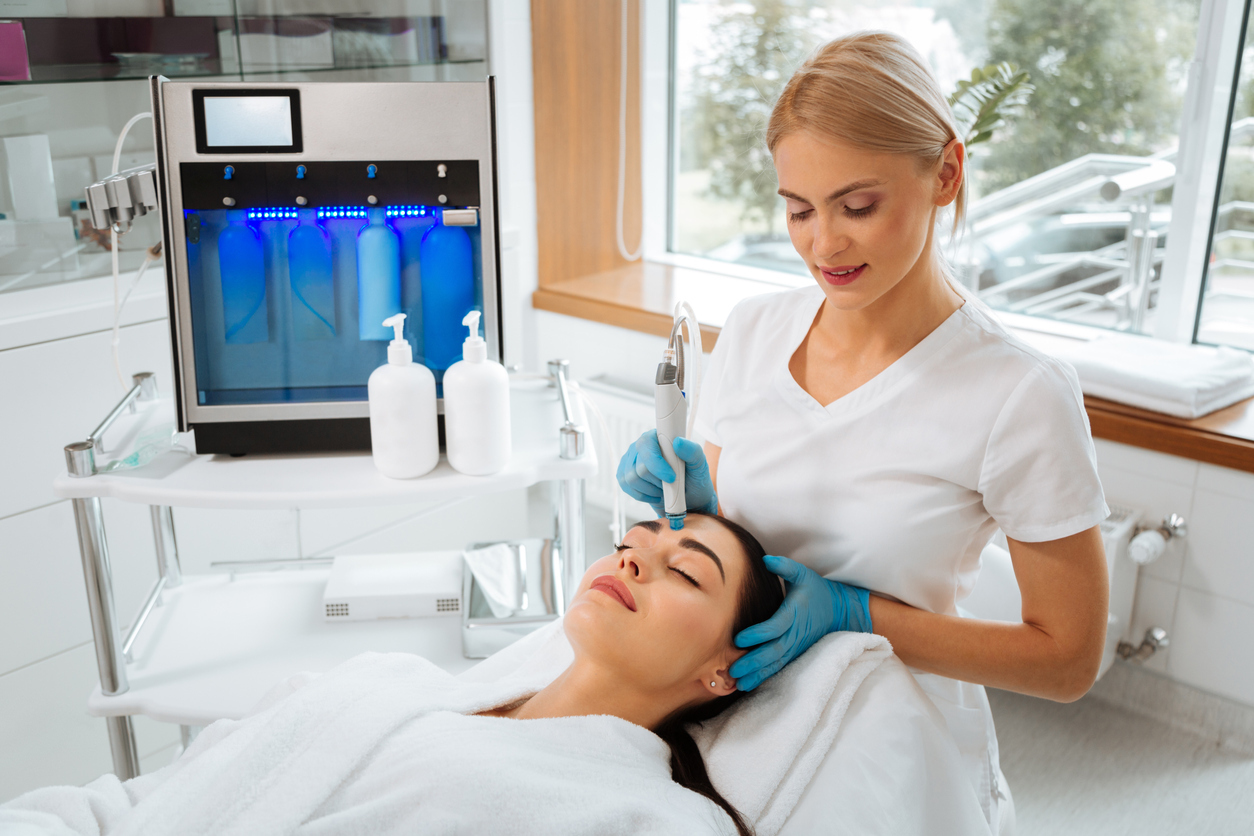 Esthetician administering HydraFacial treatment to a client’s forehead