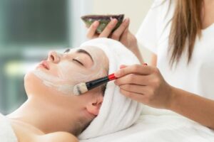 Esthetician applying a facial mask to client’s cheek using a brush 