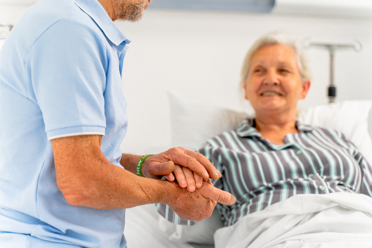 Person holding the hand of a smiling patient in a hospital bed