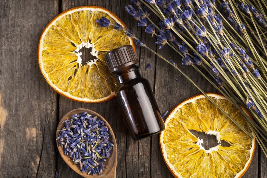 Bottle of essential oil on wooden table with dried orange slices and lavender sprigs