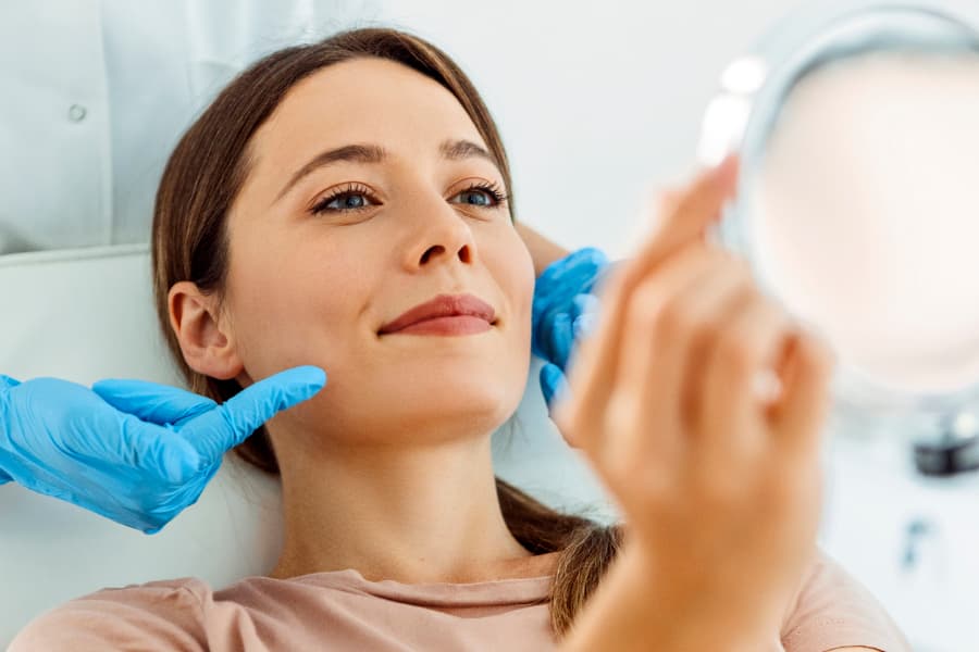 Client holding up mirror and smiling as esthetician points out hair removal area