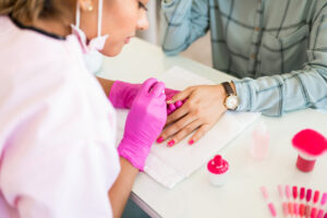 Nail technician wearing pink gloves applies nail product with client
