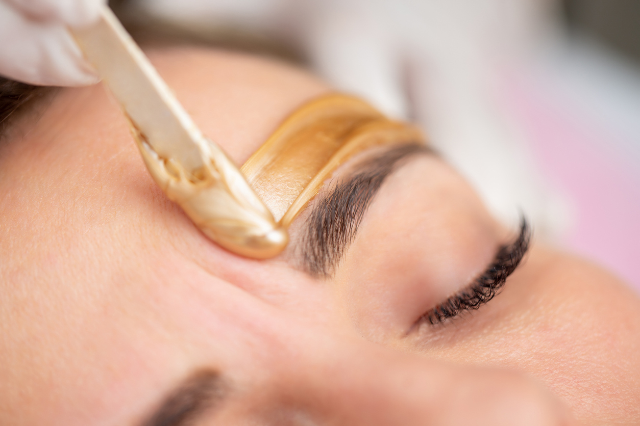 Beauty professional spreading wax above client’s eyebrow